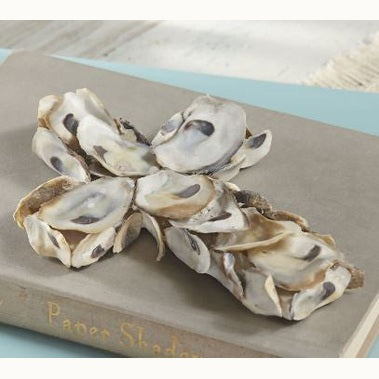 Handcrafted oyster shell sculpture of a decorative cross resting on a vintage cloth-bound book featuring iridescent pearly white interiors with dark purple muscle scars and rough tan outer edges