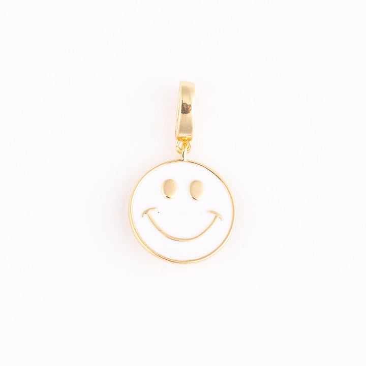 Gold and enamel jewelry charm of an iconic white smiley face centered on a plain background with polished gold trim, oval-shaped eyes, and a thin upturned smile