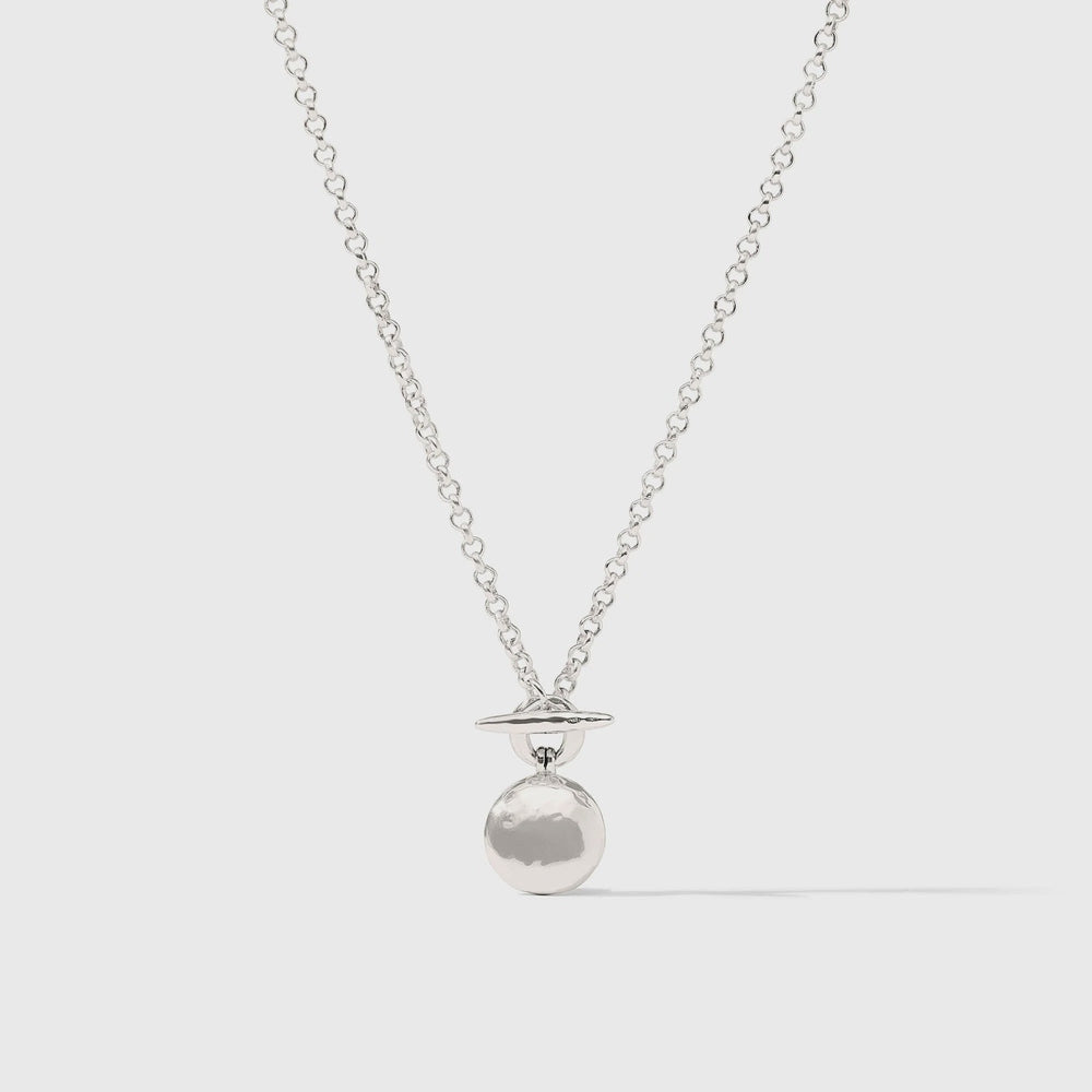 Silver-toned brass necklace by Celine featuring a Saturn-inspired pendant with a hammered-texture orb and thin horizontal ring suspended from a reflective link chain against a plain light grey background