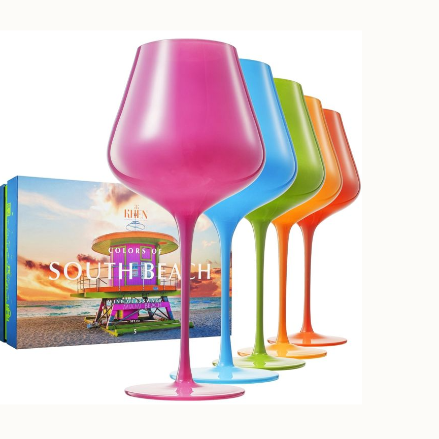 Glassware by Khen featuring five vibrant wine glasses in translucent neon hues beside packaging showcasing the iconic pink and purple 10th Street lifeguard tower at South Beach, Miami during a golden sunset