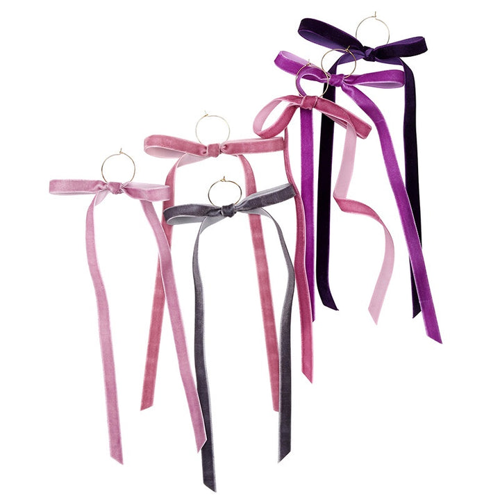 Product photography of five gold hoop earrings featuring long cascading velvet ribbons in shades of deep violet, dusty rose, and charcoal grey against a white studio background
