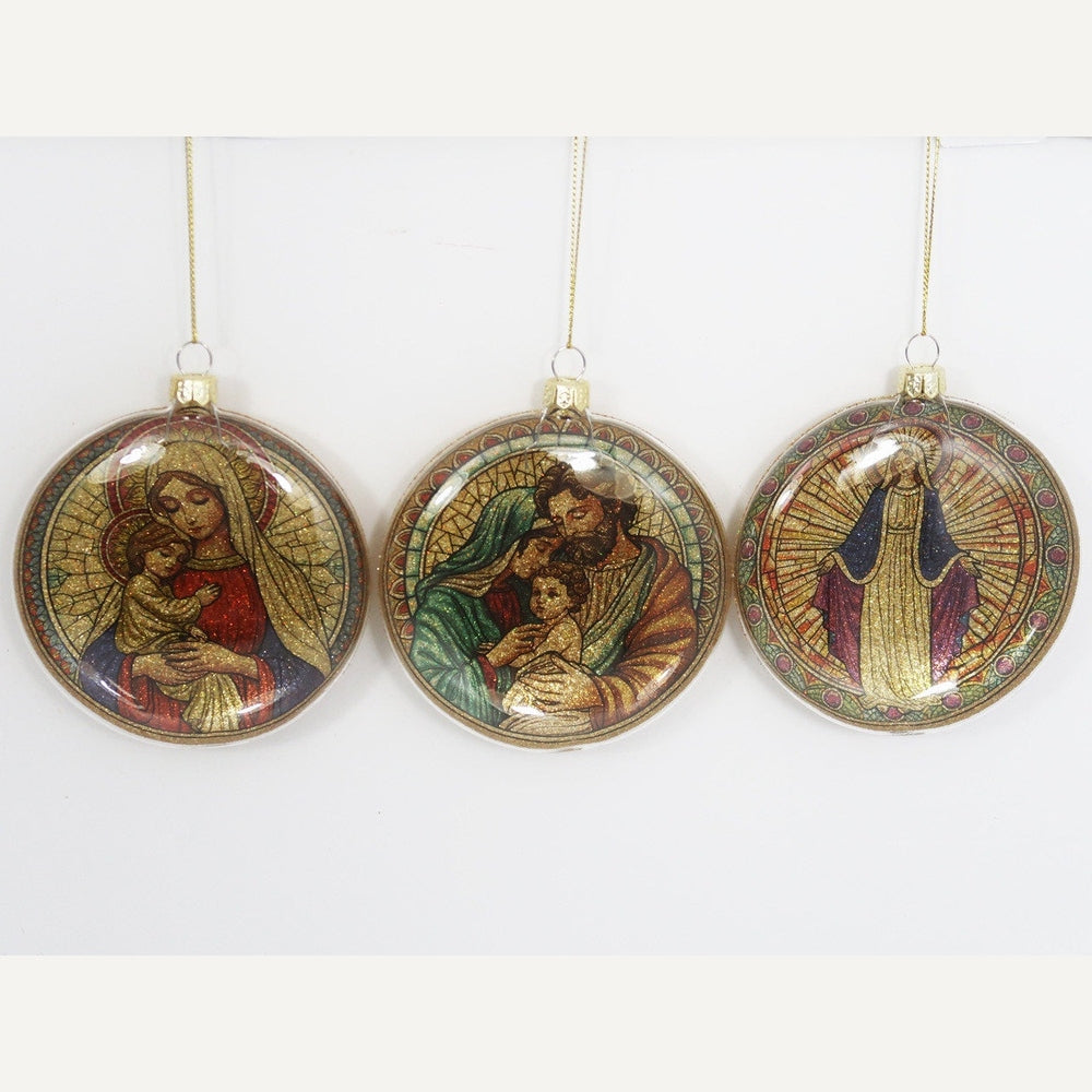 Glass Christmas ornaments featuring stained-glass style religious illustrations of the Holy Family and Virgin Mary with shimmering gold glitter backgrounds, vibrant jewel-toned mosaic patterns, and circular glass frames