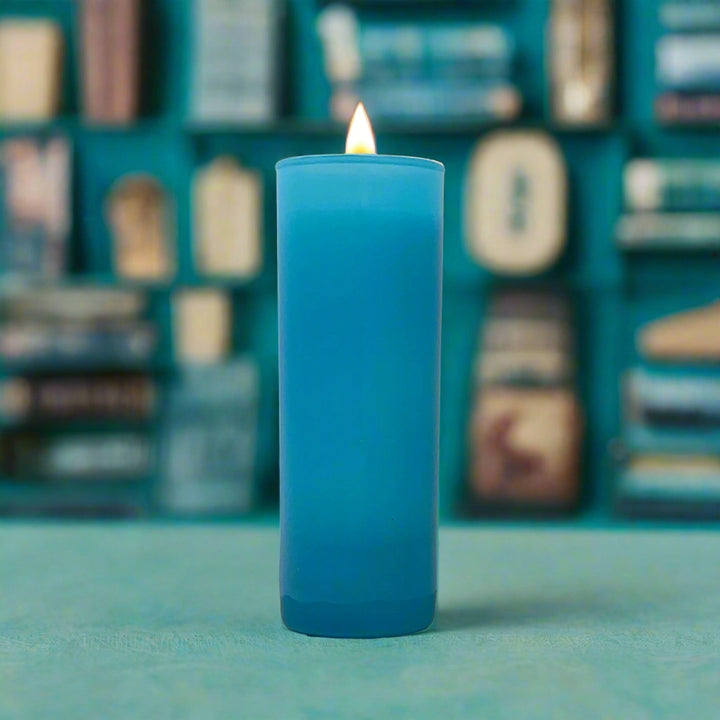 Digital photograph of a lit blue candle in a frosted glass holder set in a study featuring a vibrant yellow flame and a soft-focus background of books on teal shelves