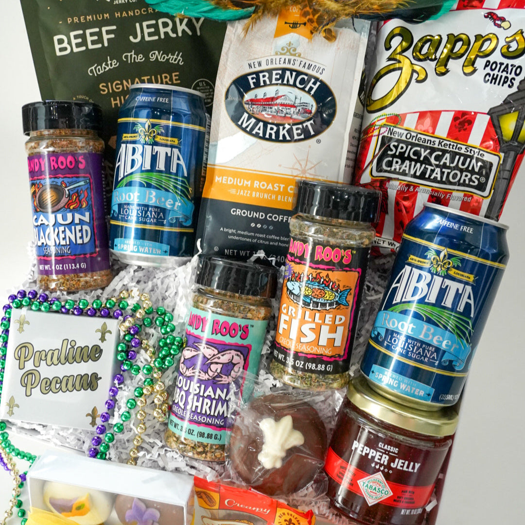 Photograph of a New Orleans culinary gift basket featuring the French Market logo, vibrant purple and green Mardi Gras beads, blue Abita Root Beer cans, and spicy Zapp&