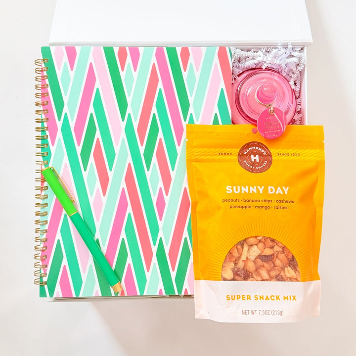 Notebook with colorful zigzag pattern, pink candle, and snack mix on a white background