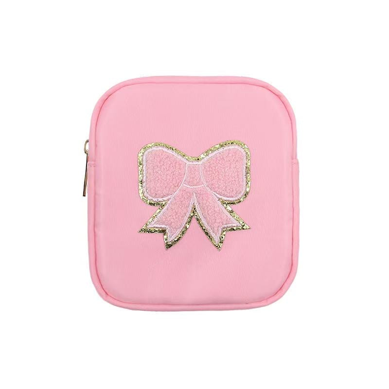 Nylon travel accessory by Stoney Clover Lane featuring a light pink square pouch on a white background with a textured chenille bow patch outlined in sparkling gold glitter and a gold-toned side zipper