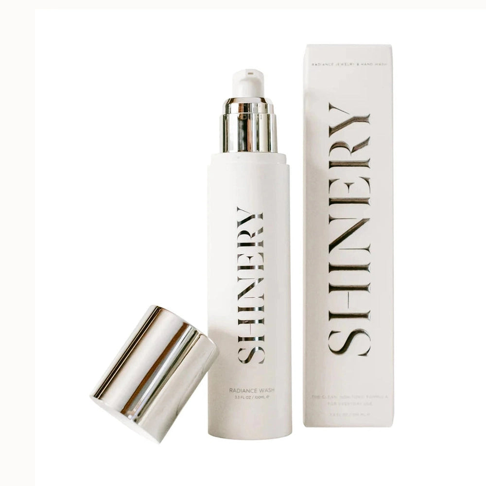 Product photography by Shinery of a Radiance Wash jewelry and hand wash set against a white background featuring bold black vertical typography, a sleek silver pump, and a detached reflective chrome cap next to a tall white packaging box