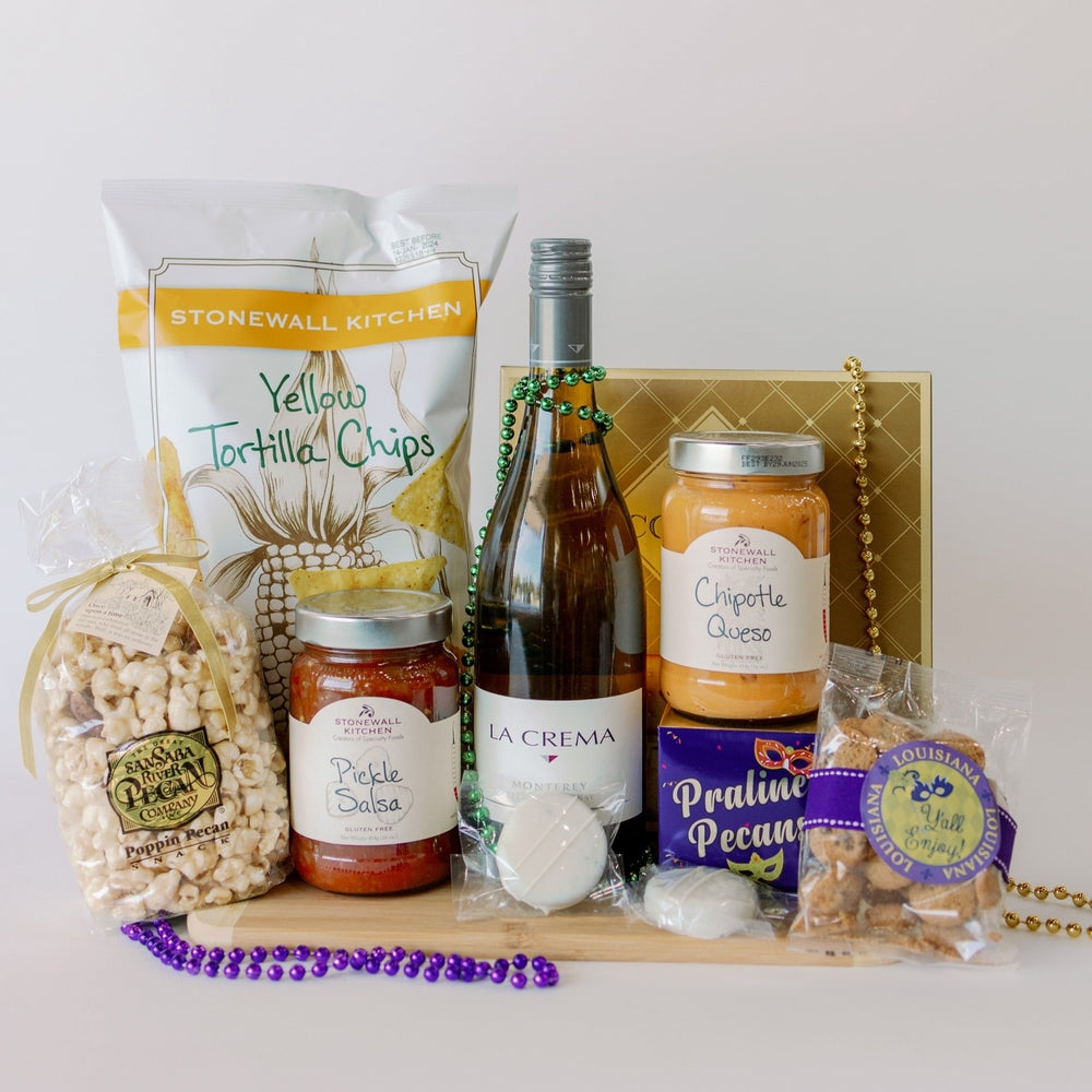 Photograph of a Mardi Gras themed gourmet gift arrangement on a wooden board featuring a bottle of La Crema wine, Stonewall Kitchen yellow tortilla chips, and jars of pickle salsa and chipotle queso accented by vibrant purple and green beads