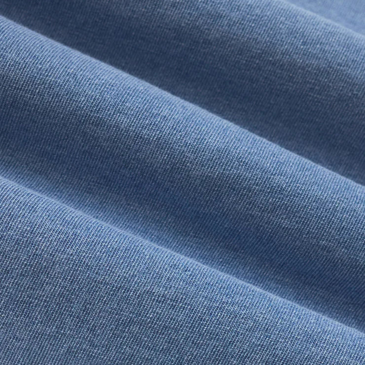 Close-up photograph of soft blue jersey cotton fabric featuring rhythmic diagonal folds, a fine knit texture, and a subtle heathered finish