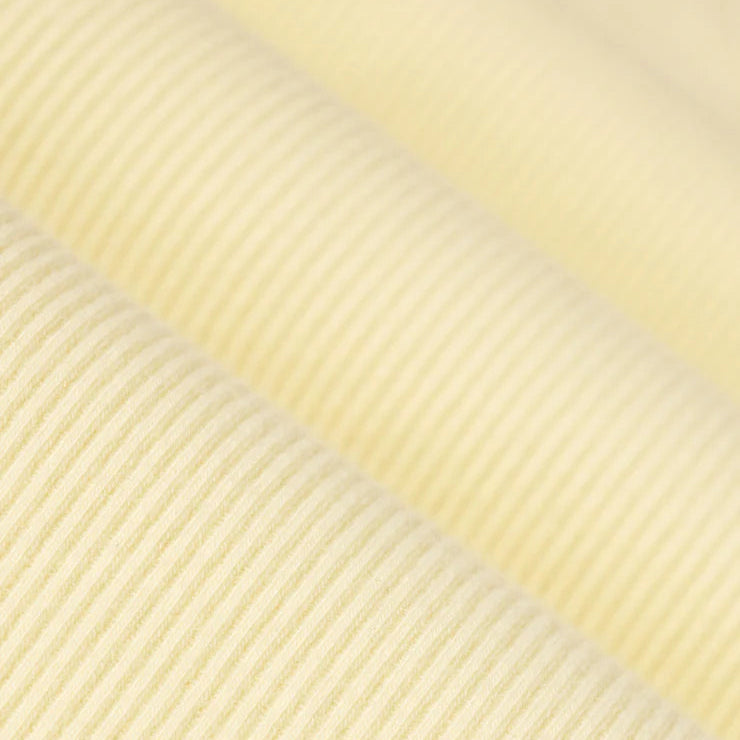 Photograph of pale yellow ribbed fabric showcasing a fine diagonal corduroy texture with soft folds that create subtle highlights and shadows across the creamy surface