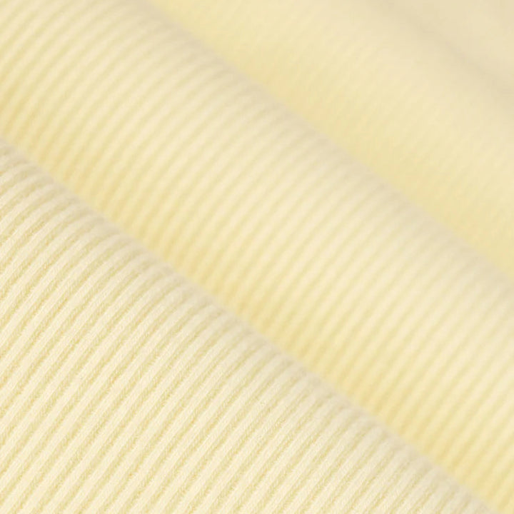 Photograph of pale yellow ribbed fabric showcasing a fine diagonal corduroy texture with soft folds that create subtle highlights and shadows across the creamy surface
