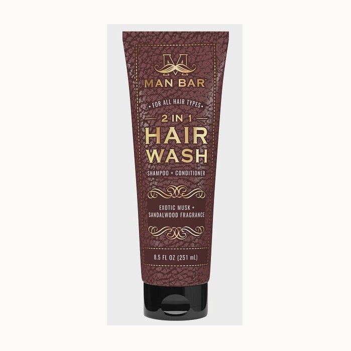 Commercial product photograph of a Man Bar 2 in 1 Hair Wash tube featuring a brown leather-textured finish, a gold mustache logo, and elegant foil typography with ornate scrollwork details