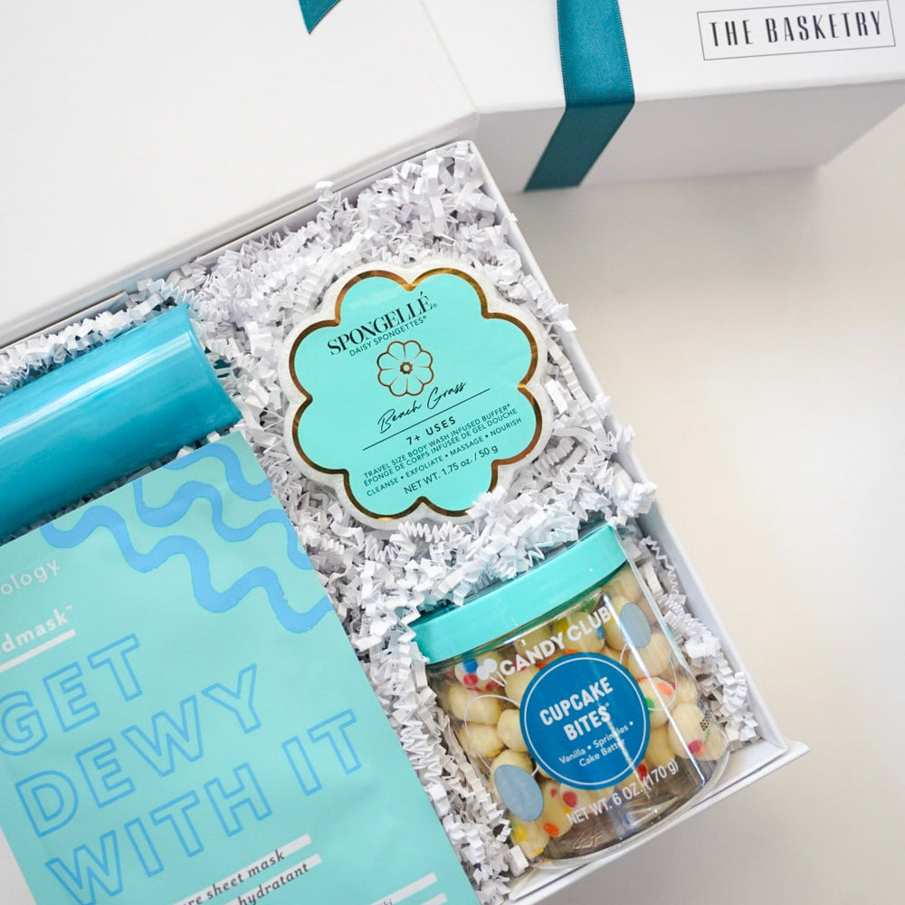 Gift set with a teal ribbon, skincare product, and snacks on a white surface