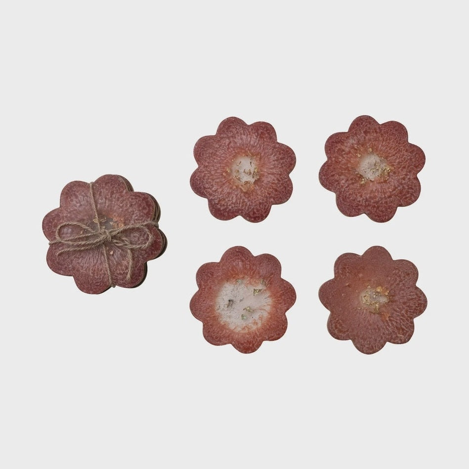 Resin coasters by an unidentified artist featuring flower-shaped scalloped edges with mauve-red pigment, metallic gold leaf centers, and a stack bound in rustic jute twine on a white background