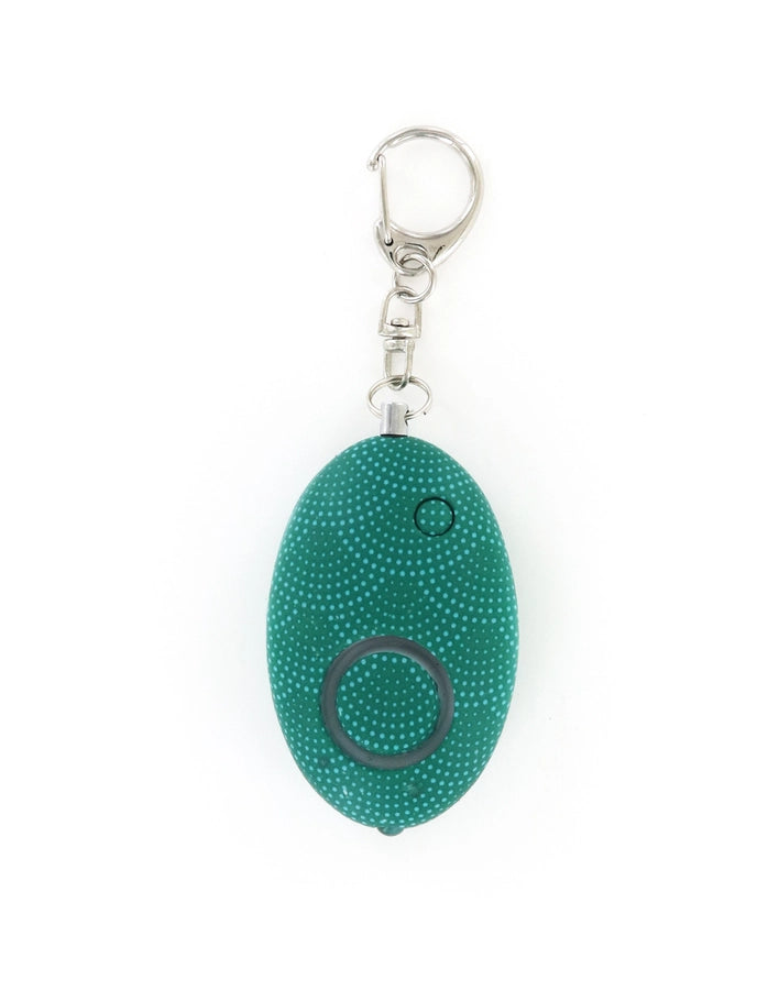 Studio product photograph of a teal oval-shaped personal safety alarm keychain on a plain white background featuring a light-colored polka dot pattern and a silver metal lobster clasp attachment