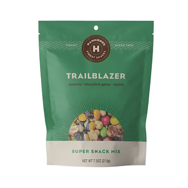 Product packaging design by Hammond’s Finest Snacks featuring a forest green bag of Trailblazer Super Snack Mix on a white background with a circular brand seal and a window showcasing colorful chocolate gems, roasted peanuts, and dark raisins