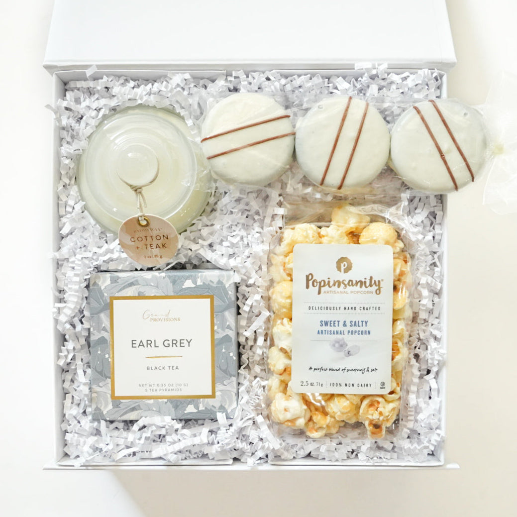 Gift set with a candle, tea, and popcorn in a decorative box on a white background