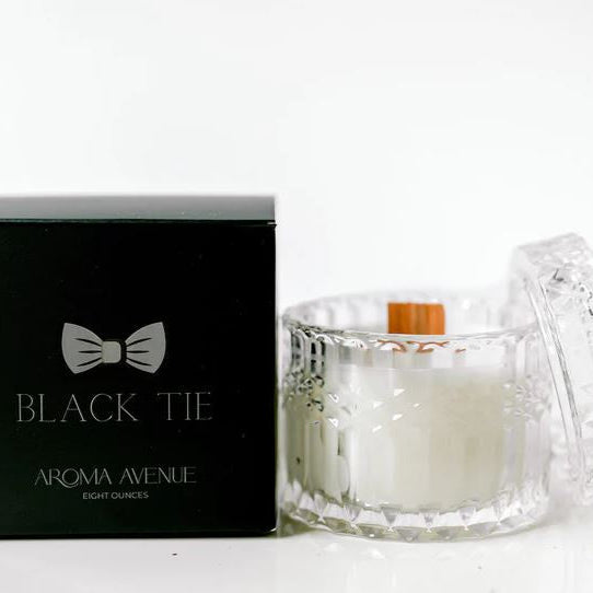 Studio photograph by Aroma Avenue of a Black Tie candle featuring a diamond-cut glass jar, a natural wooden wick, and its matching black box with a silver bow tie logo set against a white background