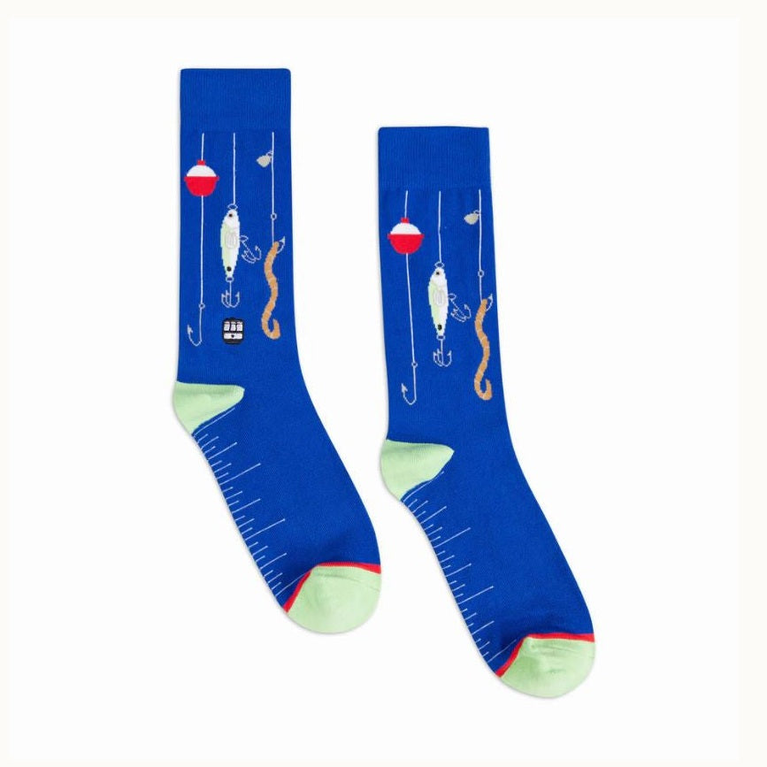 Knitted novelty crew socks featuring a fishing theme on a white background with a red and white bobber, a tan earthworm on a hook, and a white ruler measurement scale along the sole with pale green heels and toes