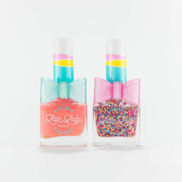 Studio photograph by Little Lady Products of two nail polish bottles on a white background featuring the brand logo, a solid coral shade with a light blue bow ring, and a colorful confetti glitter shade with a bright pink bow ring and striped caps