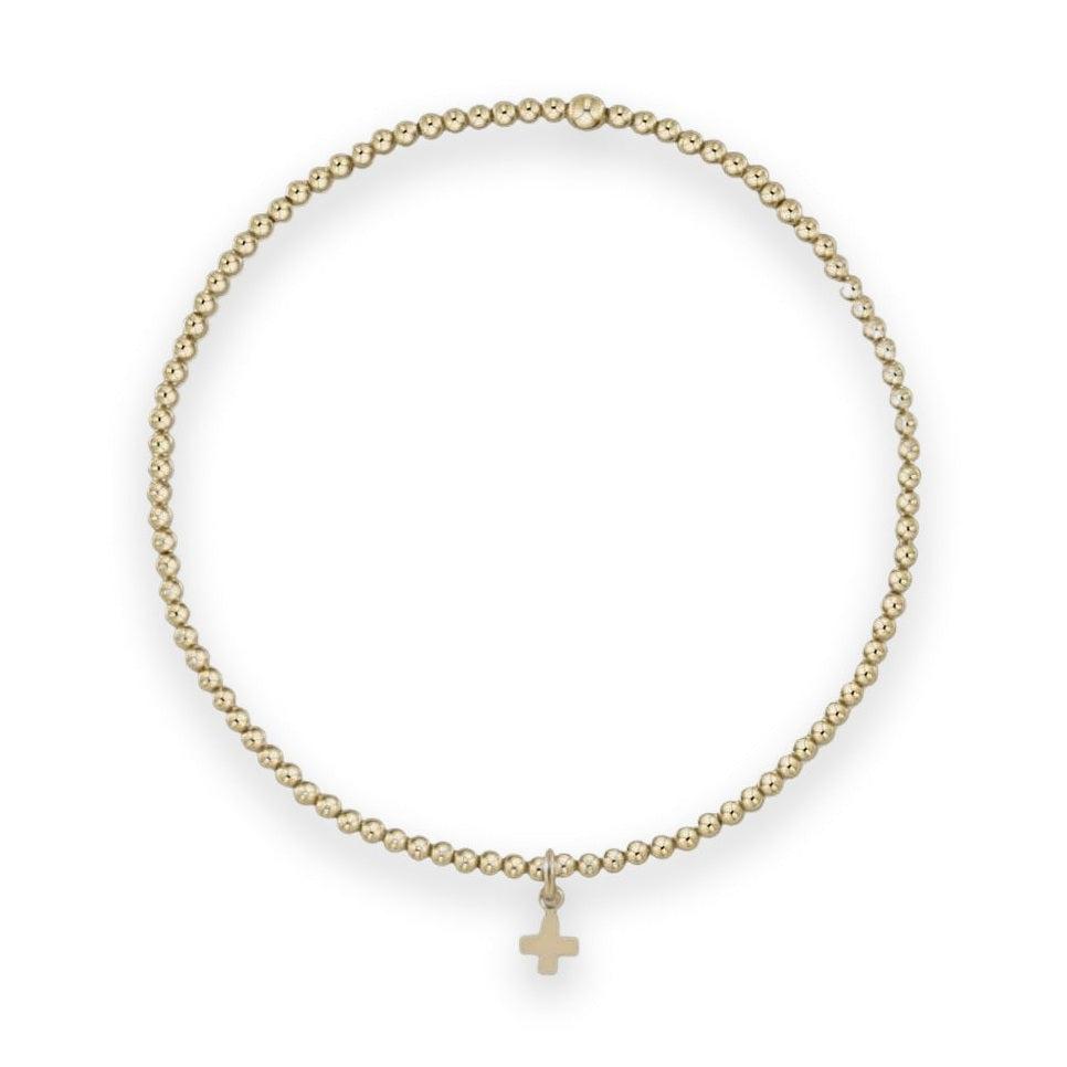 Gold-filled beaded bracelet featuring a circular strand of polished metallic spheres accented by a small dangling cross charm and a single larger bead on a neutral gray background