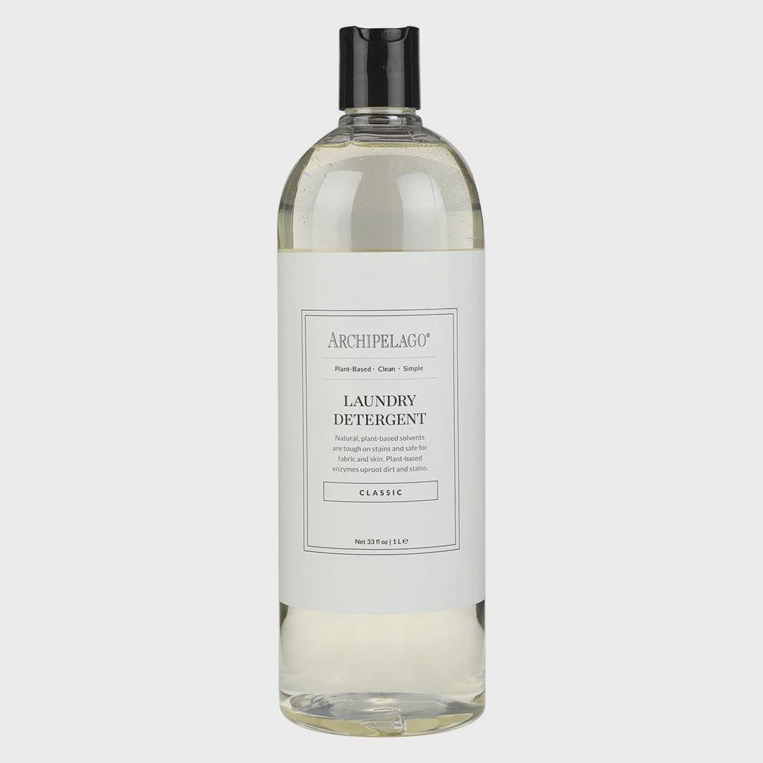 Product photograph of Archipelago Laundry Detergent in a clear 1-liter bottle featuring a black flip-top cap, a minimalist white label with the brand logo, and transparent liquid against a neutral grey studio background