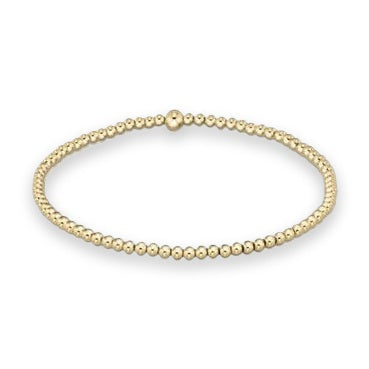 Gold beaded stretch bracelet displayed on a white studio background featuring uniform spherical beads and a single slightly larger accent bead with a high-shine reflective finish