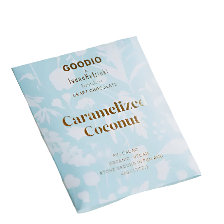 Graphic packaging design by artist Paola Suhonen for a Goodio x Ivana Helsinki Caramelized Coconut craft chocolate bar featuring a light blue floral pattern and embossed gold foil lettering on a white background