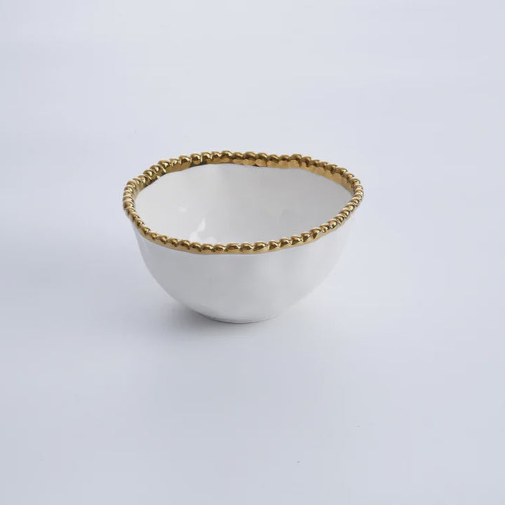 Ceramic bowl by Pampa Bay, a small white porcelain dish positioned in a minimalist studio setting featuring an organic irregular shape and a decorative gold-toned beaded rim