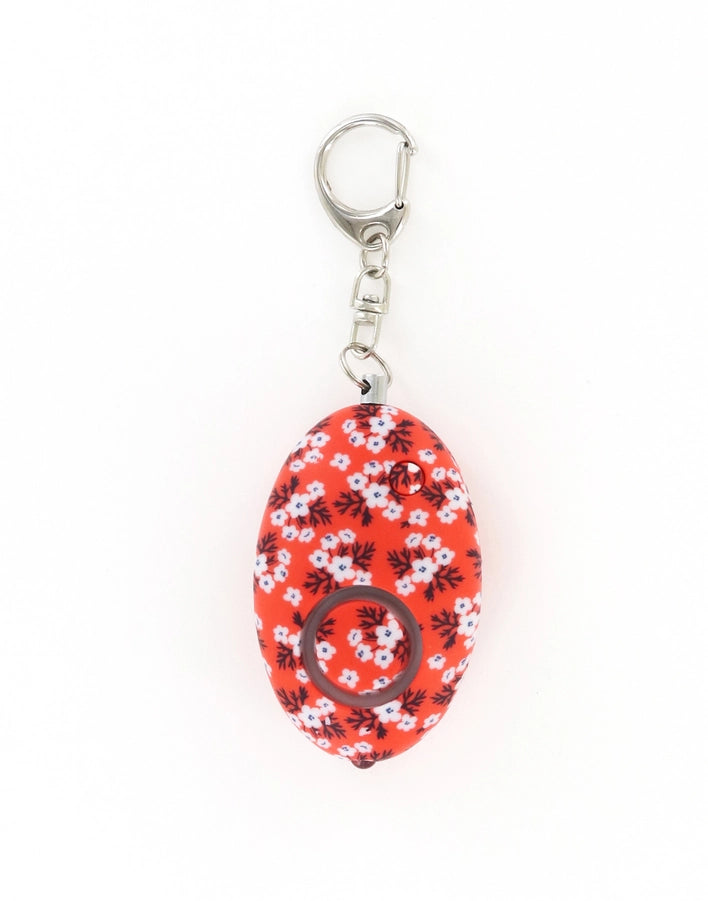 Plastic and metal personal safety alarm keychain featuring a vibrant red floral pattern with tiny white blossoms and dark foliage against a plain white background with a silver metal carabiner-style clasp