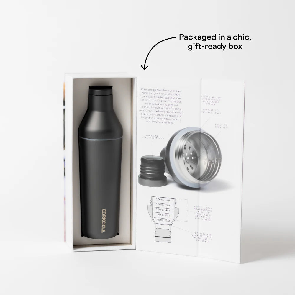 Commercial product photograph by Corkcicle of a matte black insulated cocktail shaker inside an open white gift box featuring a technical diagram of the stainless steel strainer and vertical white logo alongside promotional text highlighting the chic gift packaging