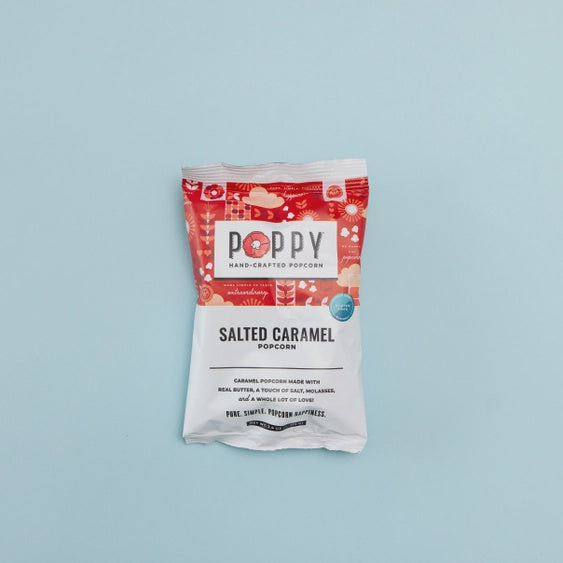 Studio photograph of a Poppy Hand-Crafted Popcorn bag centered on a light blue background featuring a vibrant red top with floral illustrations and bold black Salted Caramel typography