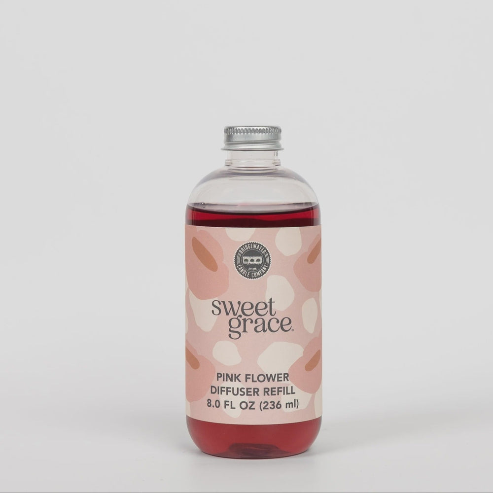 Product photography of a Bridgewater Candle Company Sweet Grace Pink Flower Diffuser Refill featuring vibrant magenta liquid, a metallic silver cap, and a pink-and-cream abstract petal label against a plain light background