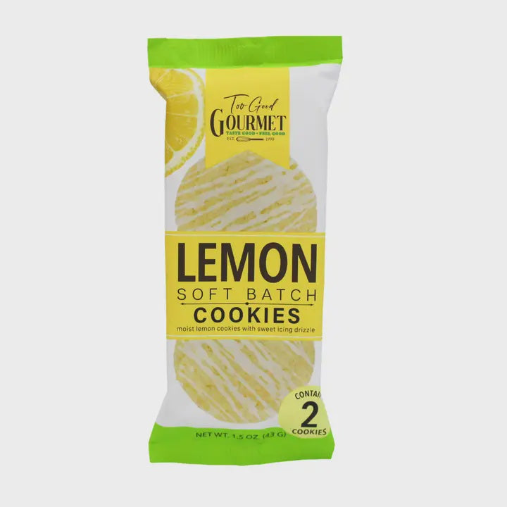 Commercial product photograph of Too Good Gourmet Lemon Soft Batch Cookies packaging on a neutral backdrop featuring a vibrant yellow lemon slice illustration, lime green borders, and two cookies with decorative white icing drizzles