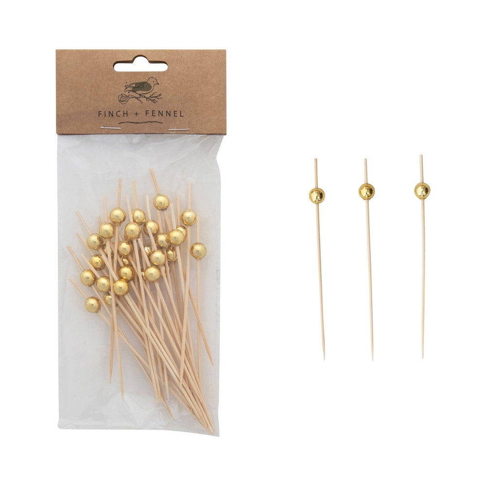 Finch + Fennel bamboo cocktail picks featuring metallic gold spherical beads packaged in a clear bag with a brown header displaying a bird logo next to three individual skewers on a white background