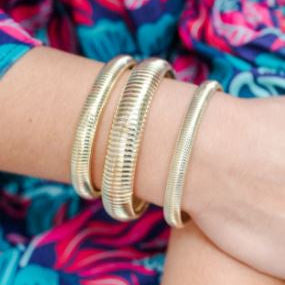Photograph of three gold-toned ribbed bracelets with a textured snake-like coil design worn on a woman&