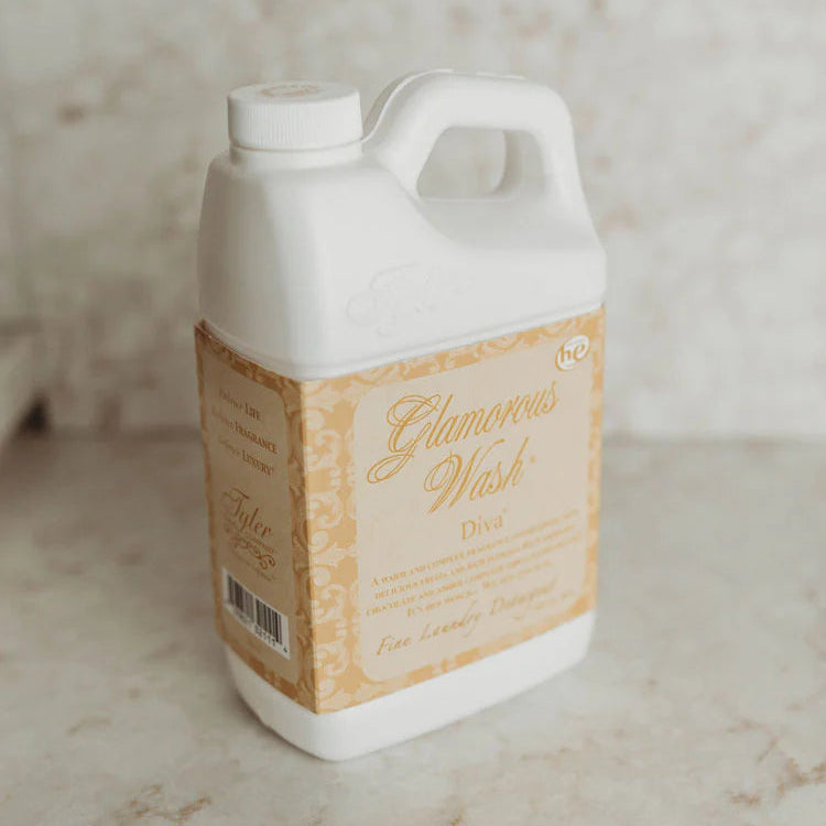 Product photograph by Tyler Candle Company of a white jug of Glamorous Wash Diva fine laundry detergent on a neutral marble surface featuring an ornate gold patterned label and elegant cursive typography