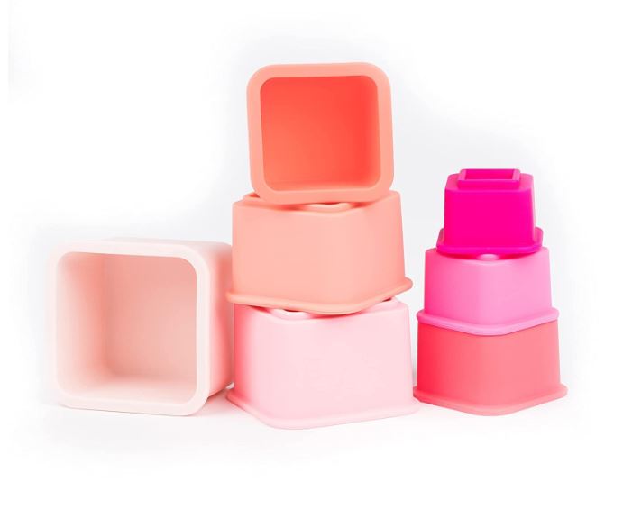 Studio photography of silicone nesting toys on a white background featuring square-shaped stacking blocks in a vibrant gradient of fuchsia, soft coral, and pale pink with smooth matte finishes