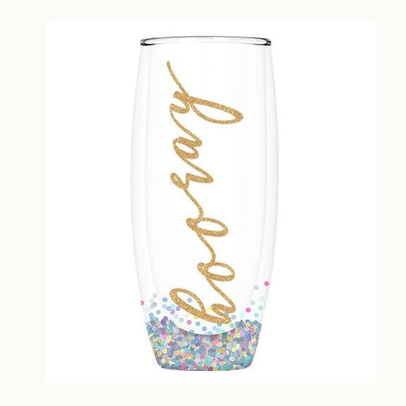 Product photograph of a clear double-walled stemless champagne flute featuring vertical gold glitter hooray script and colorful confetti sequins at the base against a white background