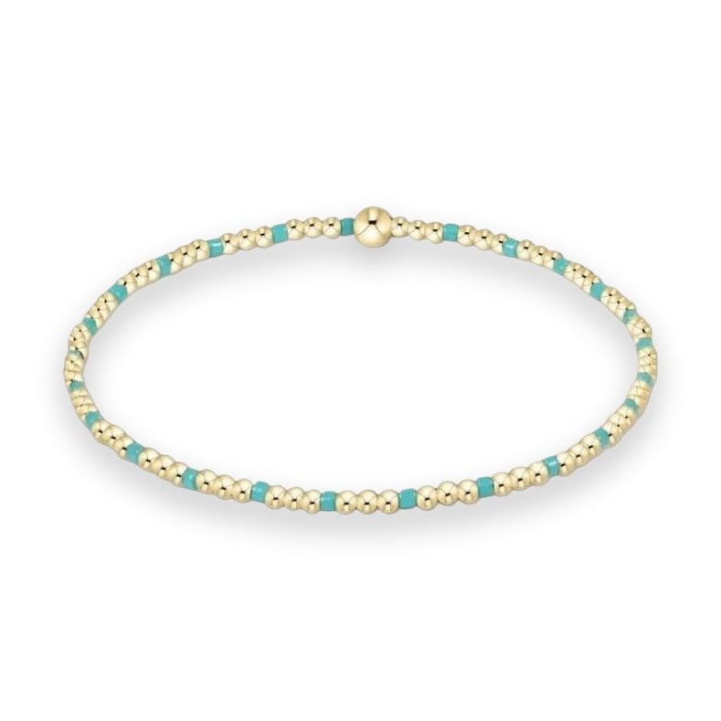 Gold and turquoise beaded bracelet by BaubleBar displayed on a white studio background featuring a repeating pattern of small polished gold spheres, vibrant turquoise blue cylinders, and a large central gold bead focal point