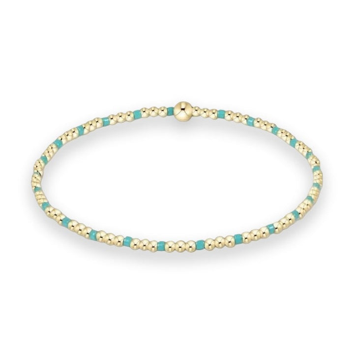 Gold and turquoise beaded bracelet by BaubleBar displayed on a white studio background featuring a repeating pattern of small polished gold spheres, vibrant turquoise blue cylinders, and a large central gold bead focal point