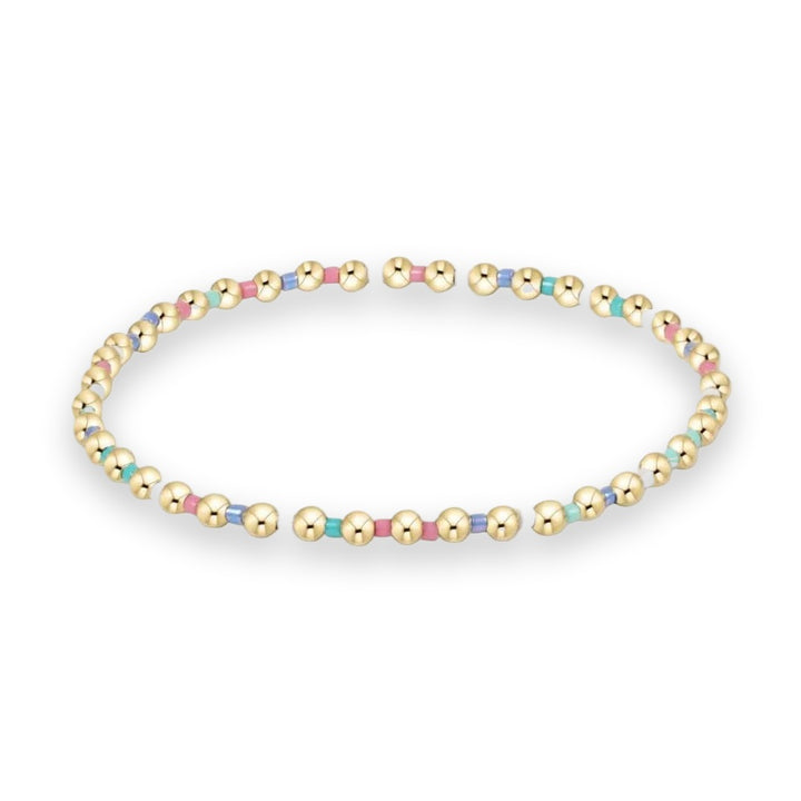 Gold-toned beaded jewelry bracelet isolated on a white background featuring polished round spheres and colorful square-cut accents in pastel pink, turquoise, and white