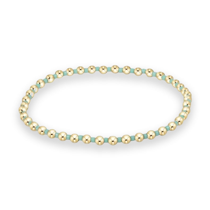 Beaded jewelry piece featuring a pattern of polished gold-filled spherical beads and matte turquoise cylindrical spacers arranged in a circular loop against a white background