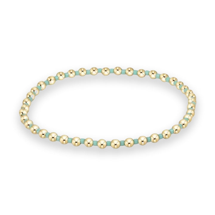 Beaded jewelry piece featuring a pattern of polished gold-filled spherical beads and matte turquoise cylindrical spacers arranged in a circular loop against a white background