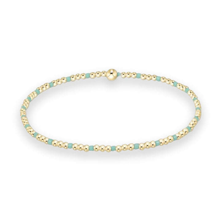 Gold-filled beaded bracelet by enewton displayed on a white studio background featuring polished spherical beads alternating with square turquoise enamel spacers and a central signature logo bead