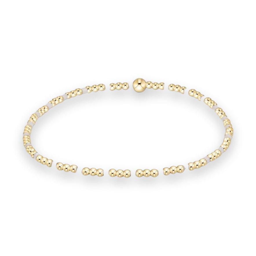 Gold-plated beaded bracelet featuring small polished spheres, cylindrical pale lavender accent beads, and a larger central focal ball bead against a white studio background