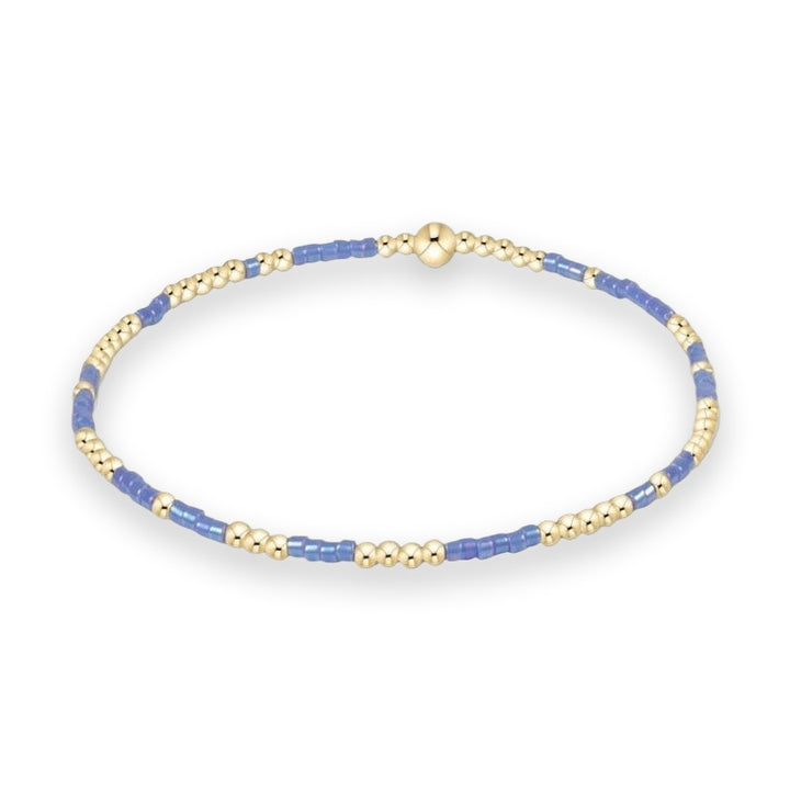 Handcrafted beaded bracelet featuring an alternating sequence of polished gold-tone spherical beads and periwinkle blue cylindrical seed beads centered with a prominent gold bead on a white background