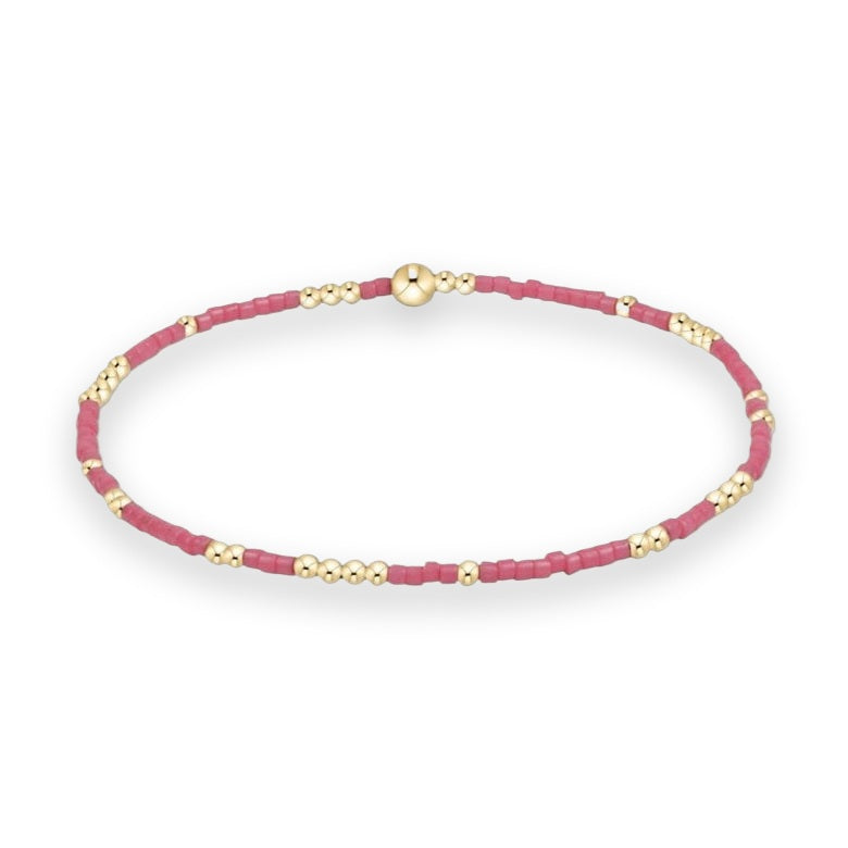 Beaded jewelry stackable stretch bracelet isolated on a white background featuring vibrant rose pink seed beads accented by polished gold-toned spherical spacers and a single larger central gold bead focal point