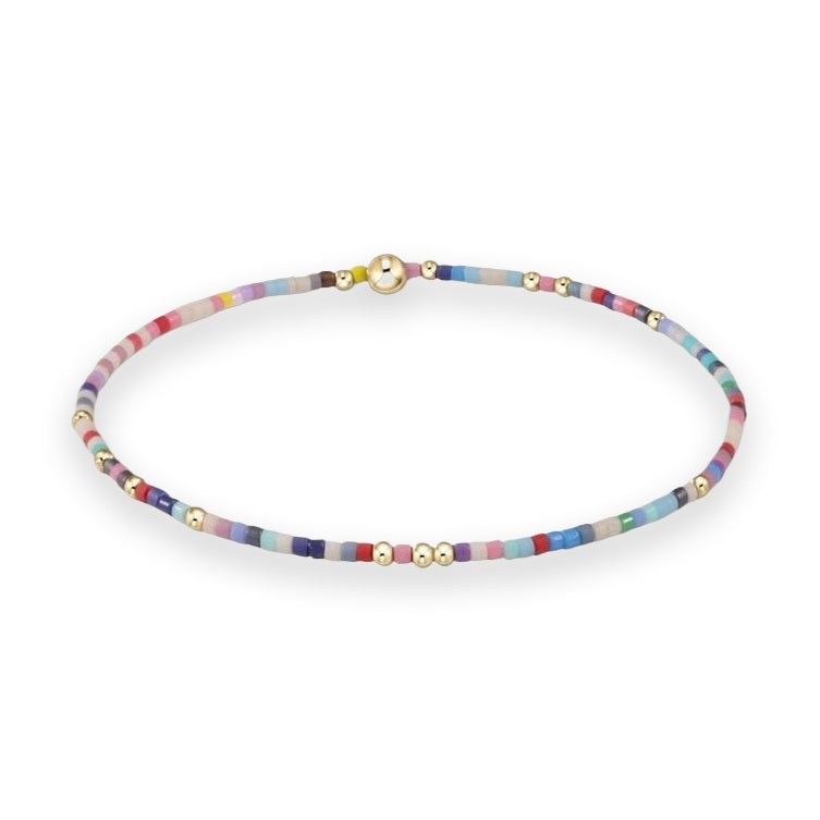Handcrafted beaded jewelry featuring a slim multicolored bracelet on a plain white background with vibrant matte seed beads, polished gold-toned spacers, and a prominent central gold-tone sphere
