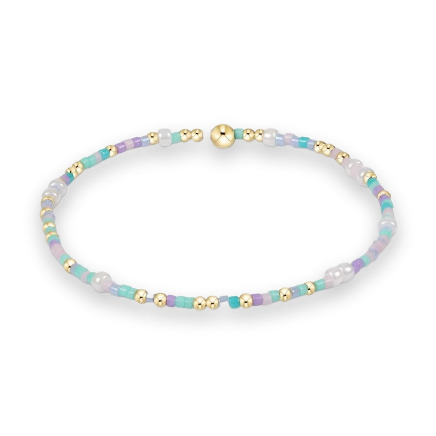 Beaded jewelry stretch bracelet on a white background featuring a colorful sequence of pastel mint, lavender, and light blue seed beads accented with polished gold metallic spheres and white faux pearls